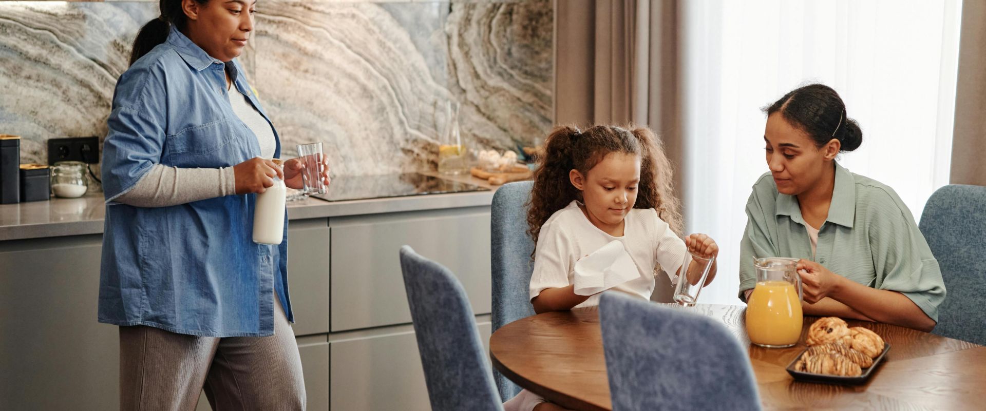 A family enjoys breakfast with pastries and drinks in a modern kitchen setting.