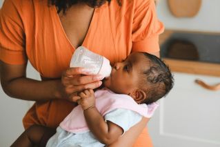 Close-up of a mother feeding her baby with a bottle in a warm home setting.